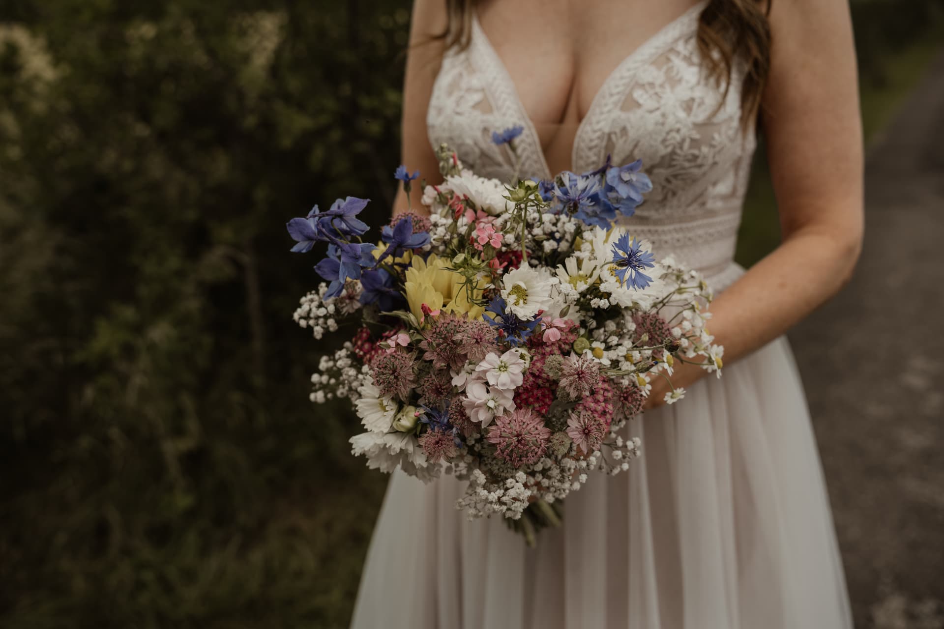 Bruid houdt veldboeket met blauwe en roze bloemen vast