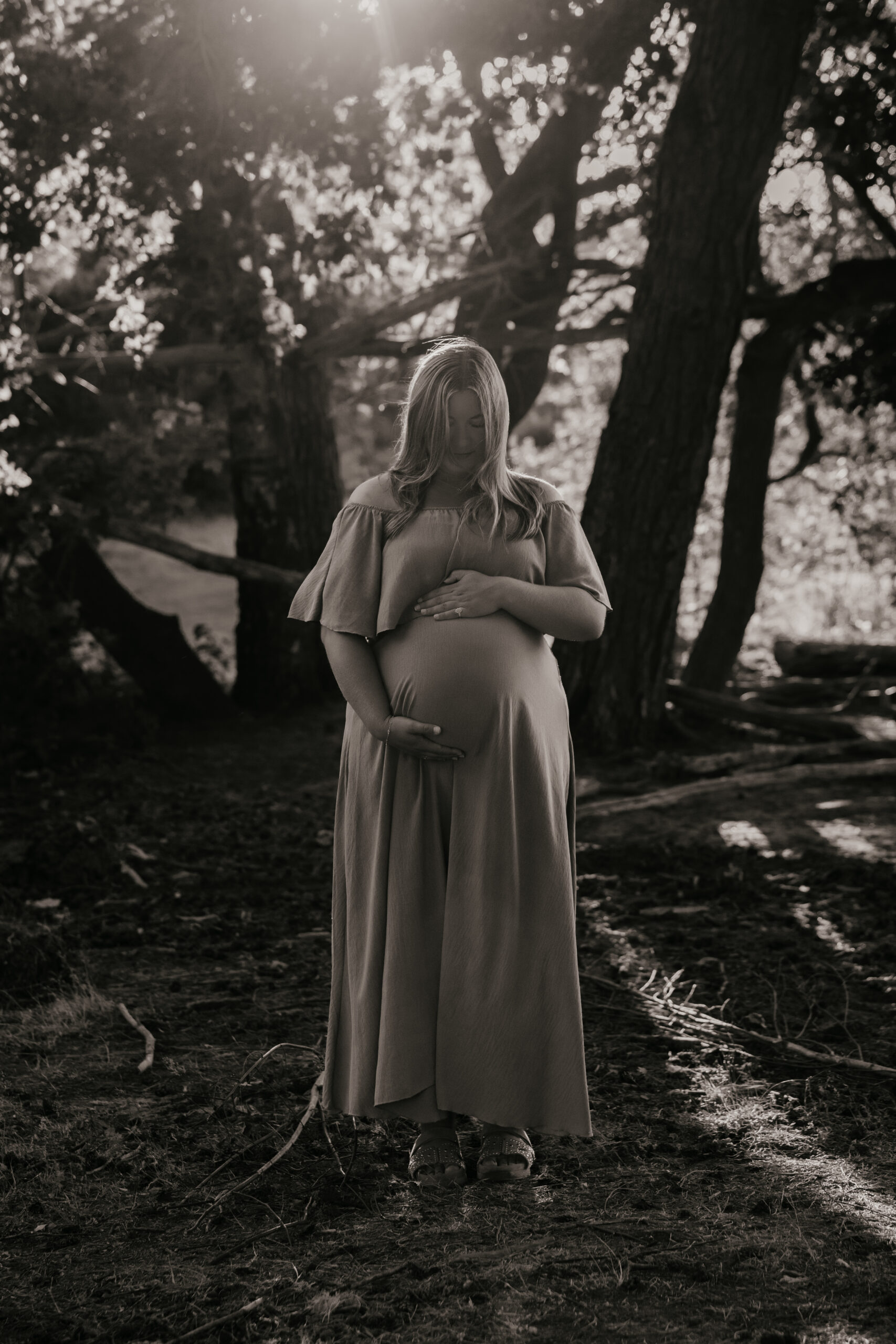 Zwart-witfoto van een zwangere vrouw met haar handen om haar buik in het bos